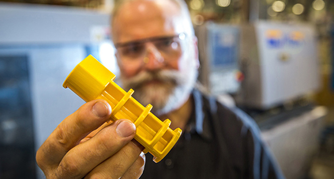 technician holding yellow injection molded part from protolabs